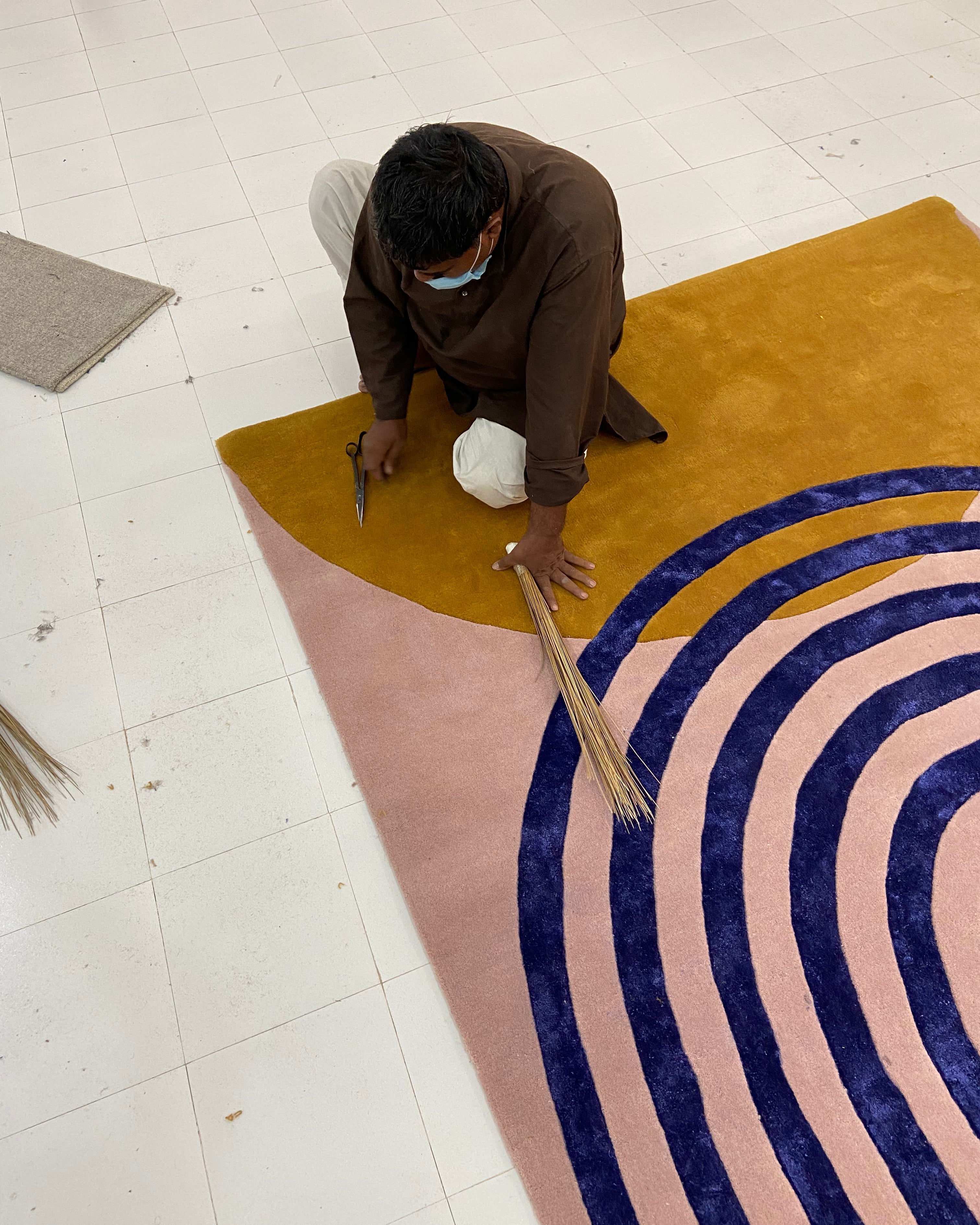 Person working on a circular patterned rug with concentric circles in a workshop setting.