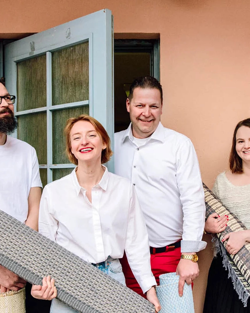 Finarte team standing together holding woven rugs in front of a building.