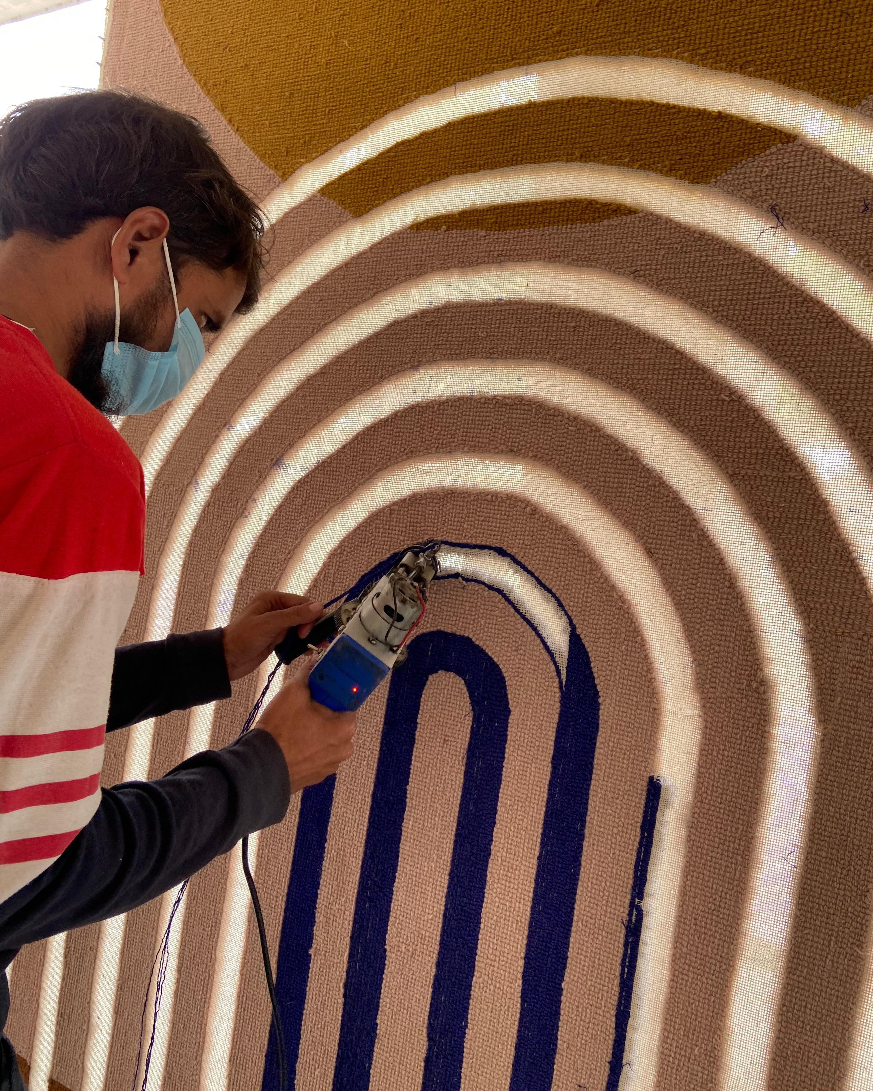 Person using a tufting tool on a circular patterned surface of a wool rug