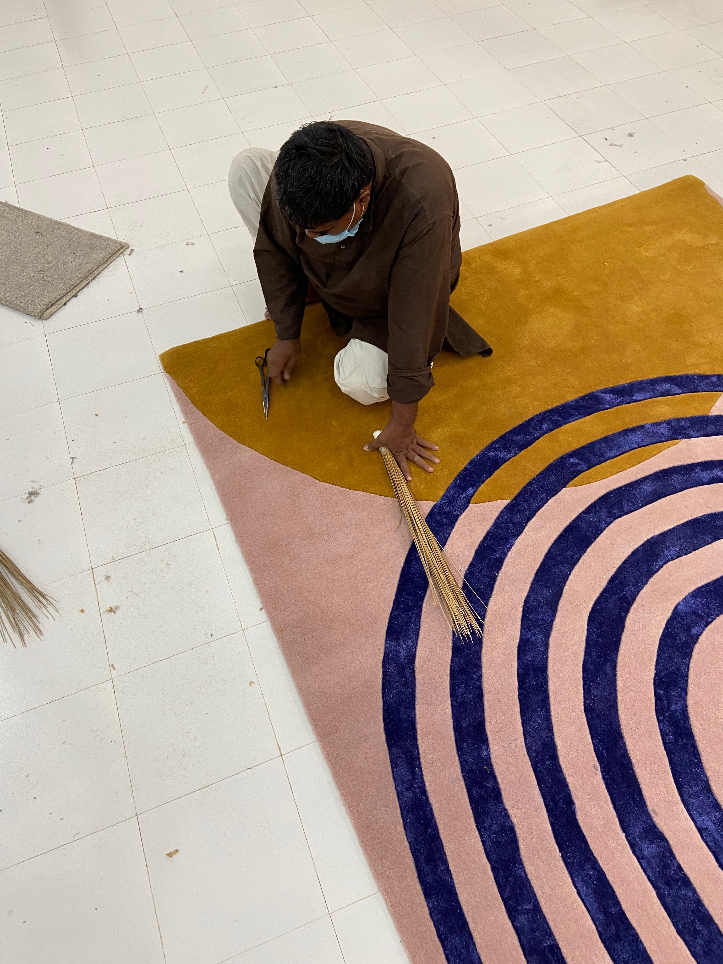 Person working on a circular patterned rug with concentric circles in a workshop setting.