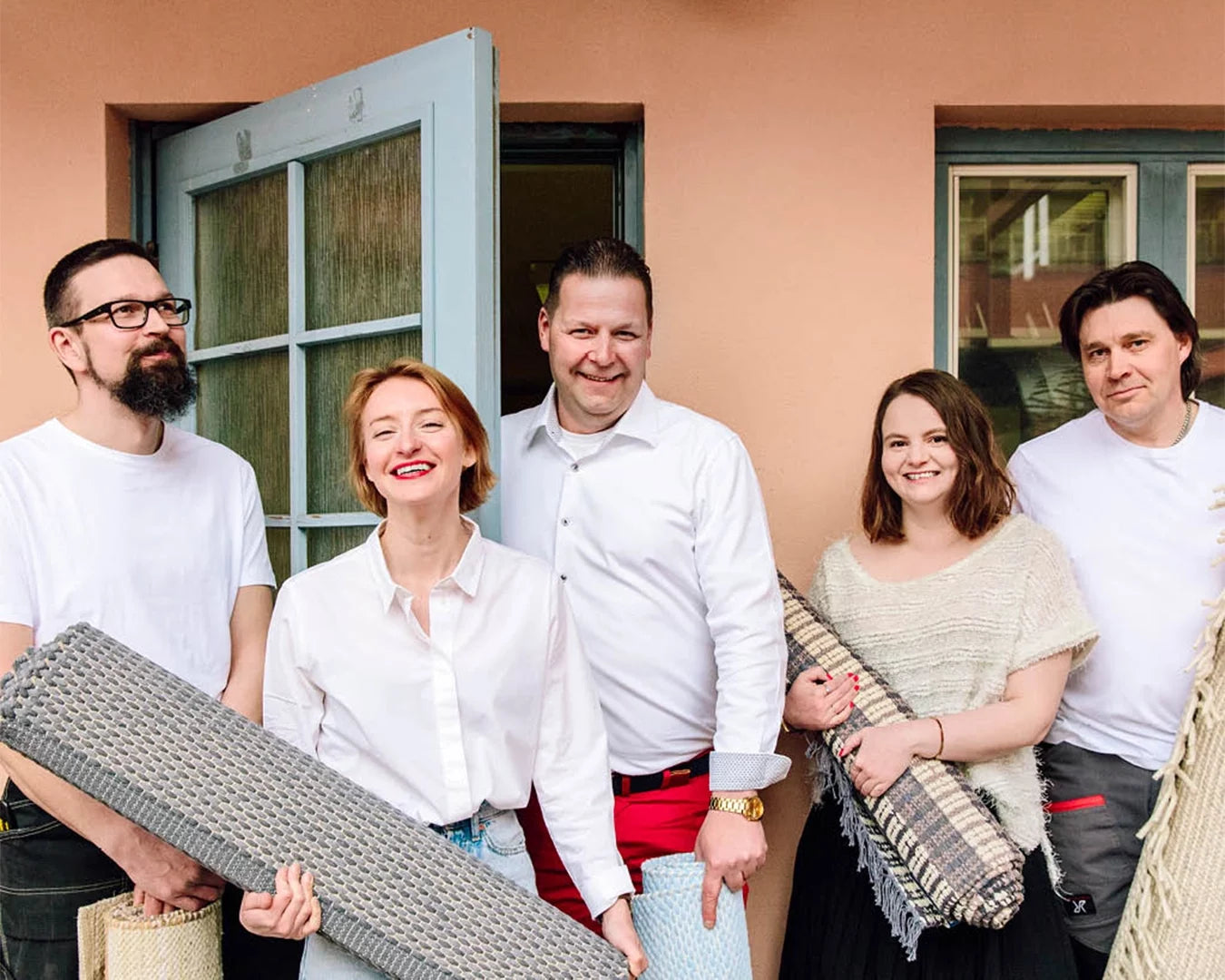 Finarte team standing together holding woven rugs in front of a building.