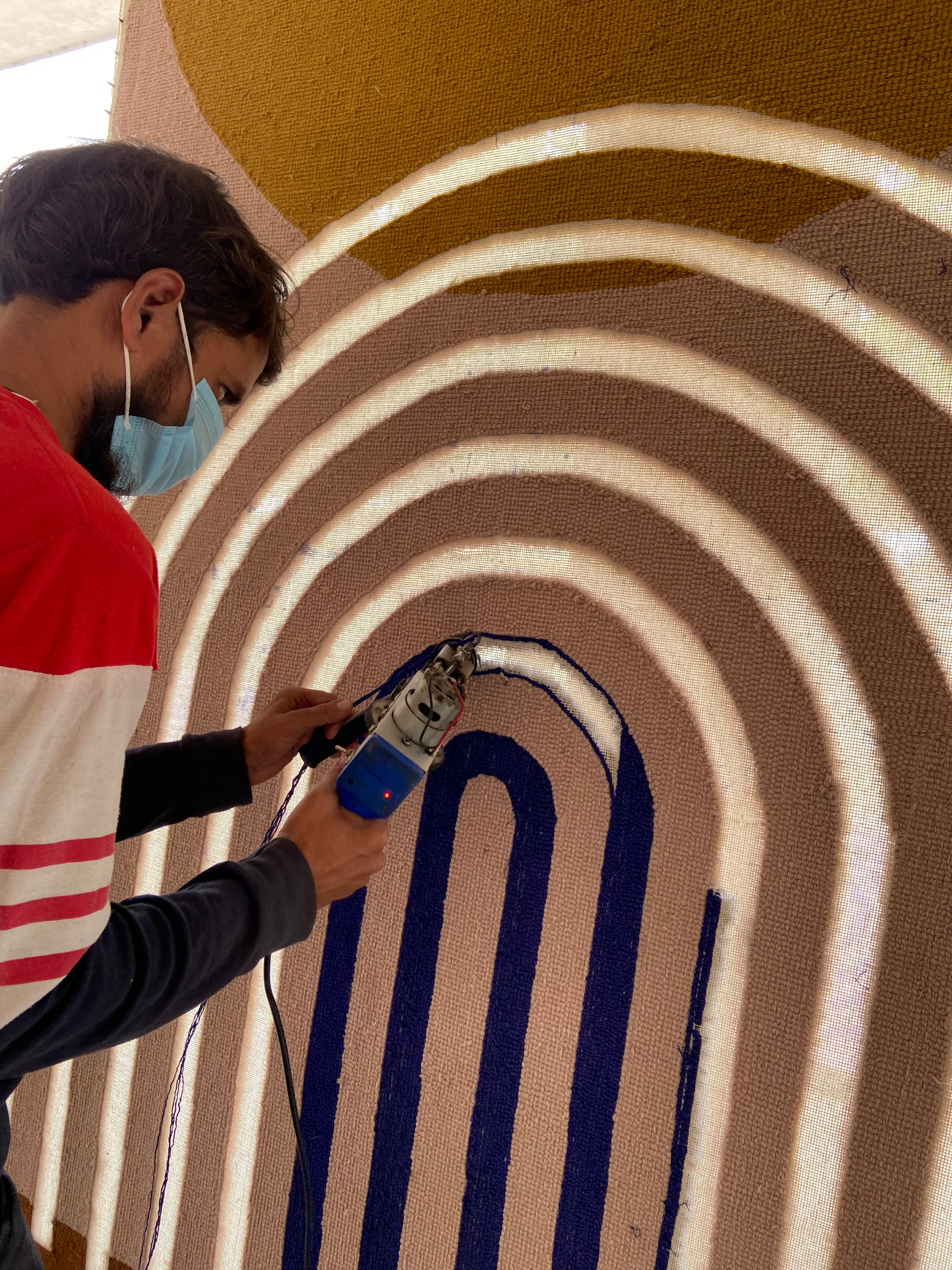 Person using a tufting tool on a circular patterned surface of a wool rug